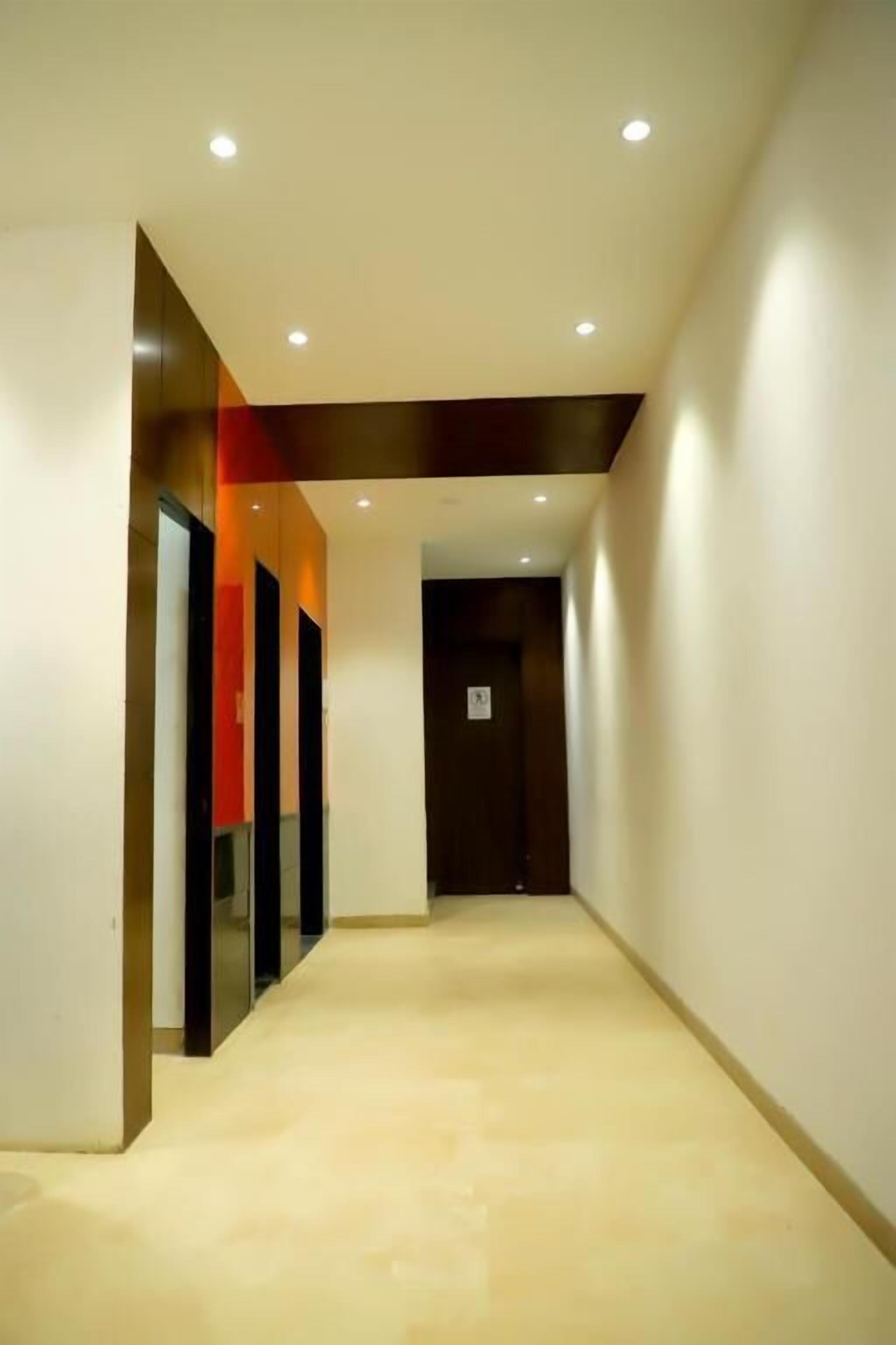 Un pasillo moderno con piso de color claro, luces empotradas en el techo y una puerta al final.