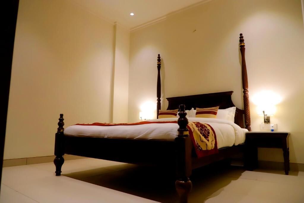 Un letto a baldacchino con struttura in legno e copripiumino rosso e giallo. Due comodini con lampade sono posti ai lati del letto.