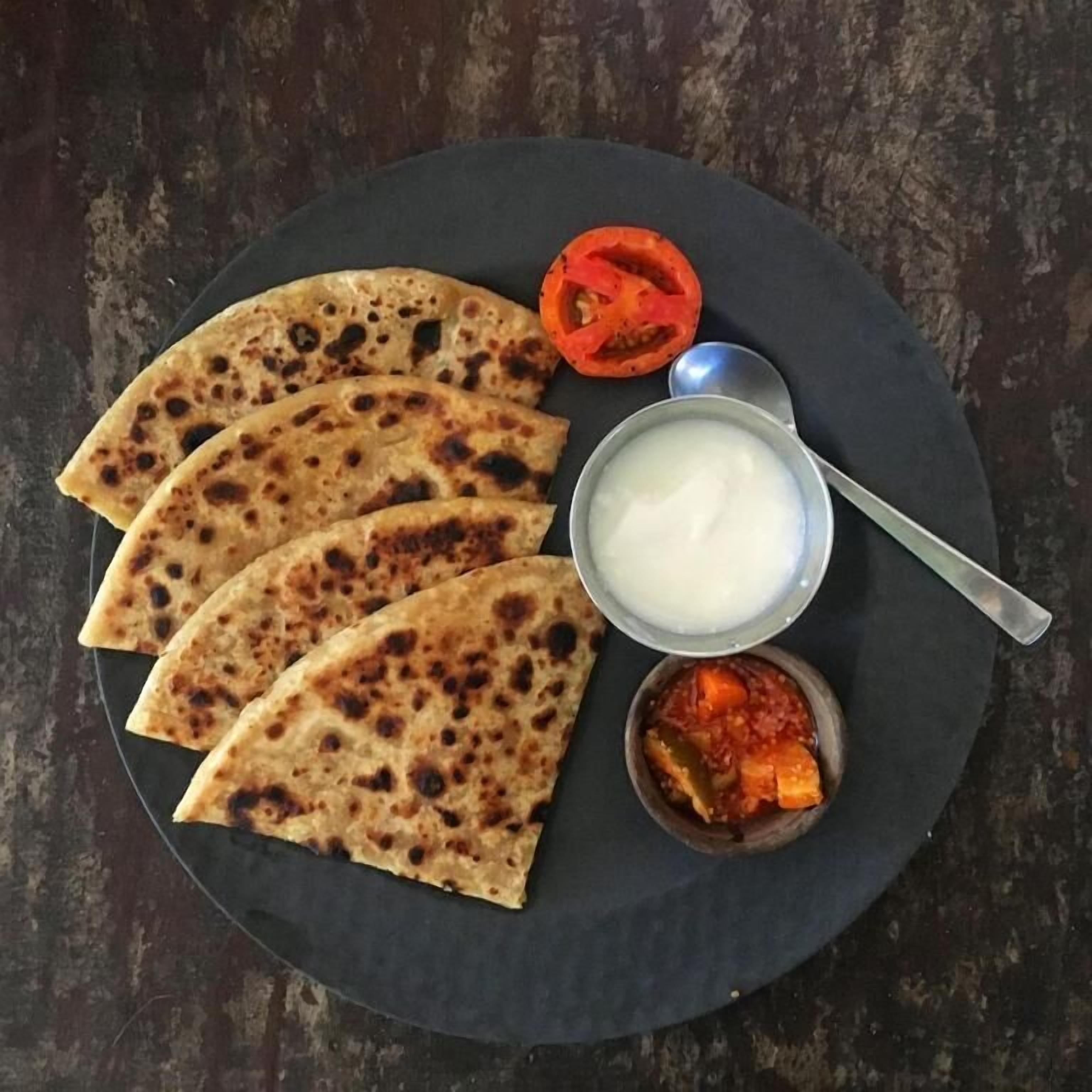 Une assiette contenant quatre morceaux de pain plat, un petit bol de sauce blanche et un bol de curry rouge.