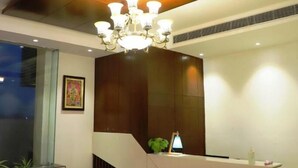 A modern reception area with a wooden reception desk, a chandelier, and a large window. - The Vrindwoods (Mathura)