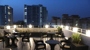 A rooftop terrace with outdoor seating, including round tables and chairs, and a laptop on one of the tables. - The Vrindwoods (Mathura)