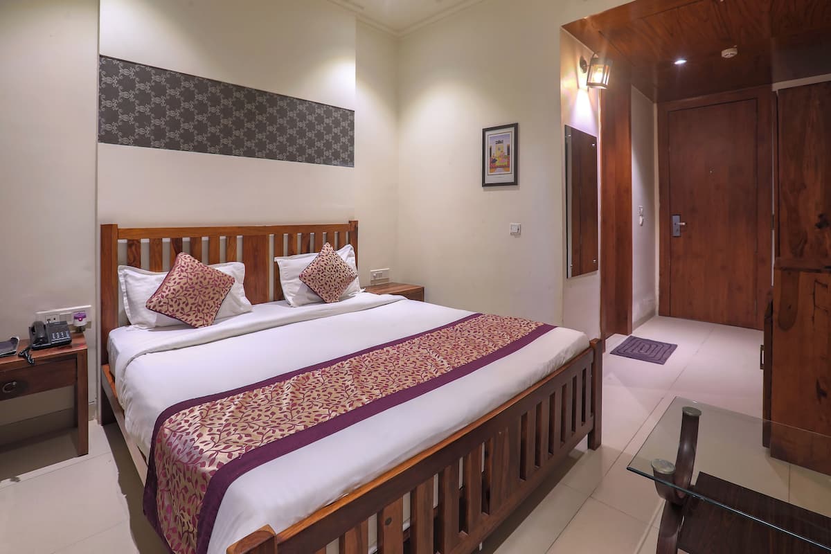 A neatly made bed with a patterned bedspread and pillows, a bedside table with a phone, and a wooden door in the background.