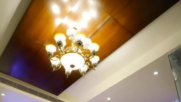 A modern lobby with a chandelier, two sofas, a small table, and large windows with a view. - The Vrindwoods (Mathura)