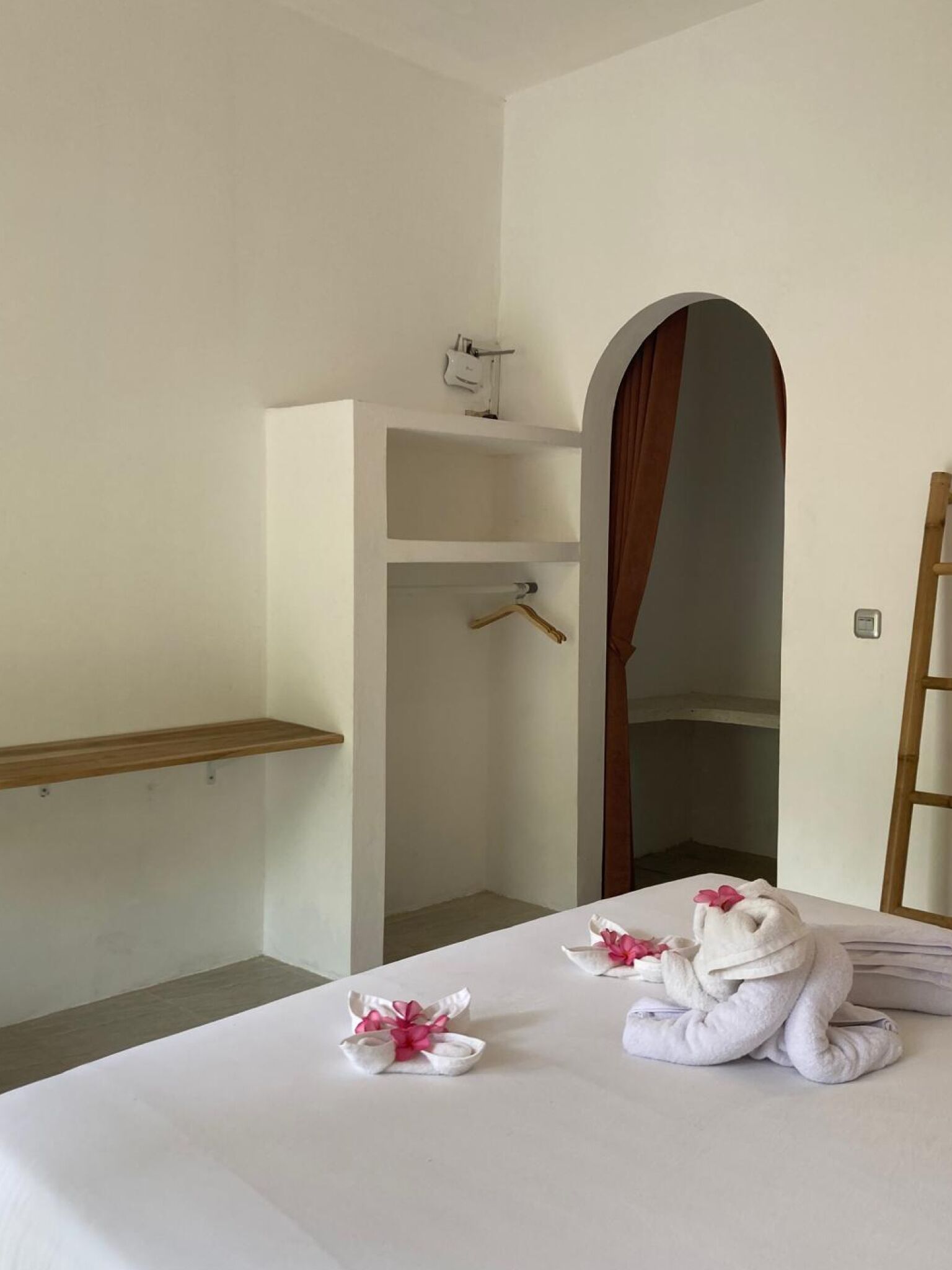 A hotel room with a bed, a wooden shelf, a wardrobe, and a mirror.
