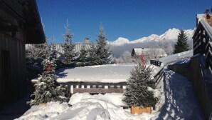 A snow-covered courtyard with wooden benches, snow-laden trees, and a mountain backdrop. - Spacious apartment with beautiful views near slopes (Villard-Reculas)