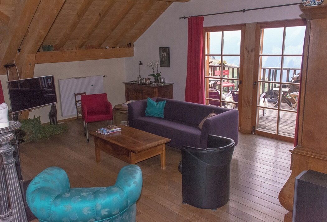 A cozy living room with a wooden ceiling, a sofa, a red chair, a coffee table, and a TV.
