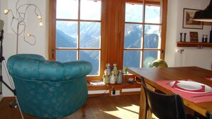A dining area with a wooden table, chairs, and a view of mountains through large windows. - Spacious apartment with beautiful views near slopes (Villard-Reculas)