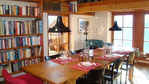 A dining area with a wooden table set for four, surrounded by bookshelves filled with books. - Spacious apartment with beautiful views near slopes (Villard-Reculas)