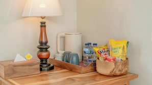 A wooden table with a tissue box, a lamp, a mug, water bottles, and snack bags. - Ashanti Guest House Ubud (Ubud)