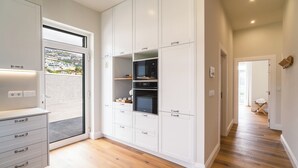 Een moderne keuken met witte kasten, inbouwovens en uitzicht door een glazen deur.