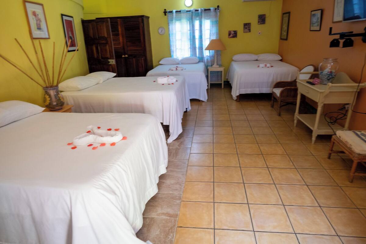 Habitación de hotel con dos camas individuales, un armario de madera, una mesita con lámpara y una silla.