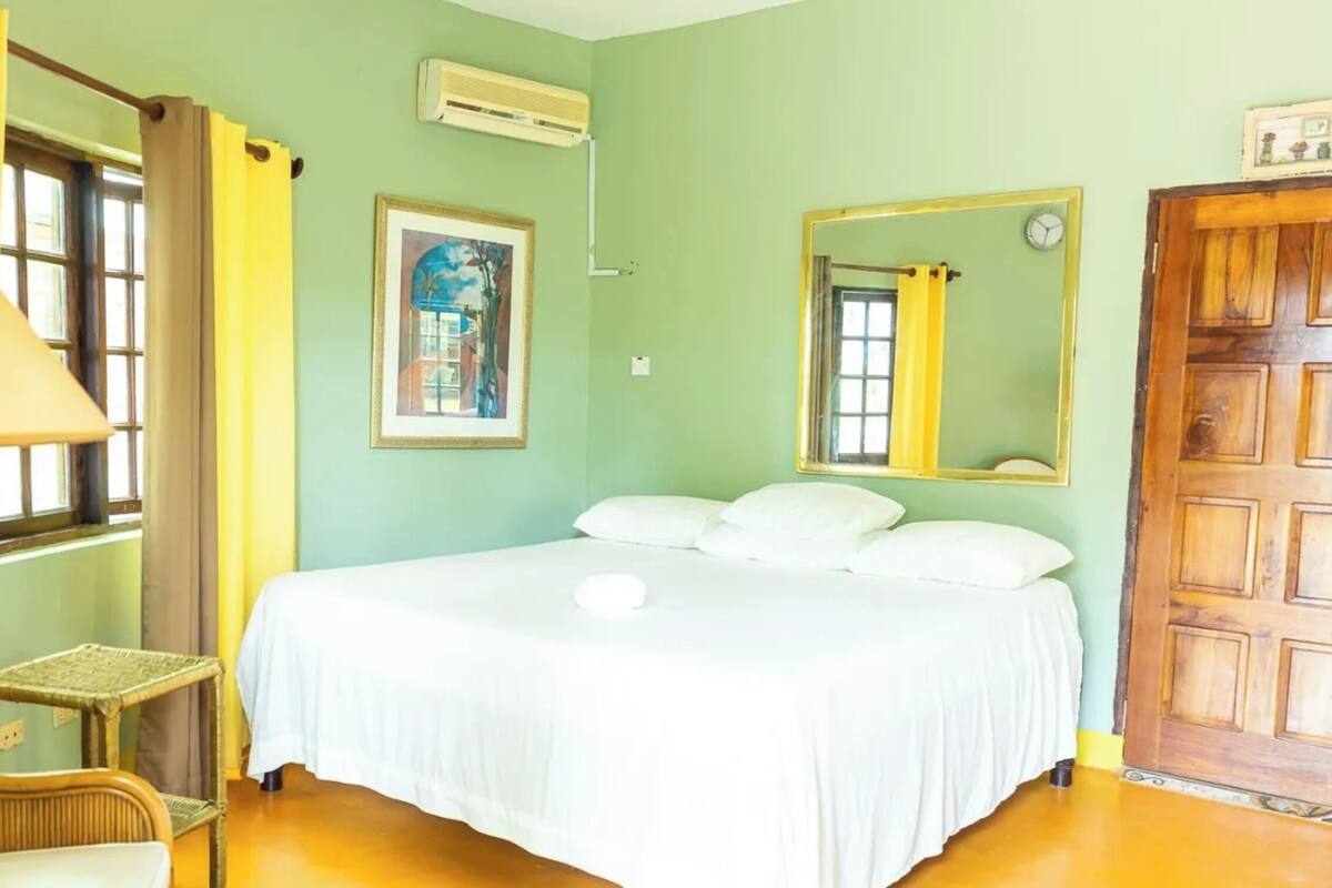 Una habitación con cama, una silla, una lámpara, un cuadro, un espejo y una puerta.