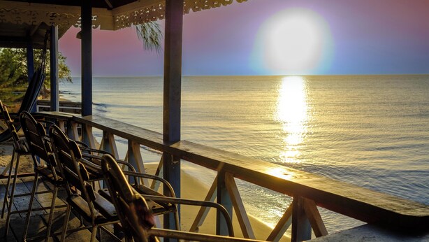 Una terraza de madera con barandillas metálicas que da a un mar tranquilo al atardecer.
