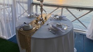 Una mesa preparada para una comida con vista al atardecer sobre el agua.