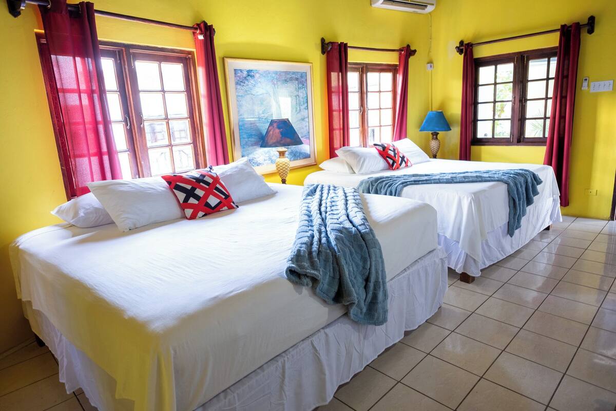 Habitación de hotel con dos camas, cortinas rojas, un cuadro y una lámpara.