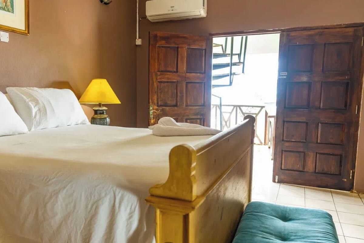 Una cama bien hecha con sábanas blancas, una lámpara de noche y un cabecero de madera.