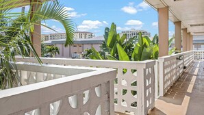 A balcony with a white lattice railing, palm trees, and buildings in the background.
