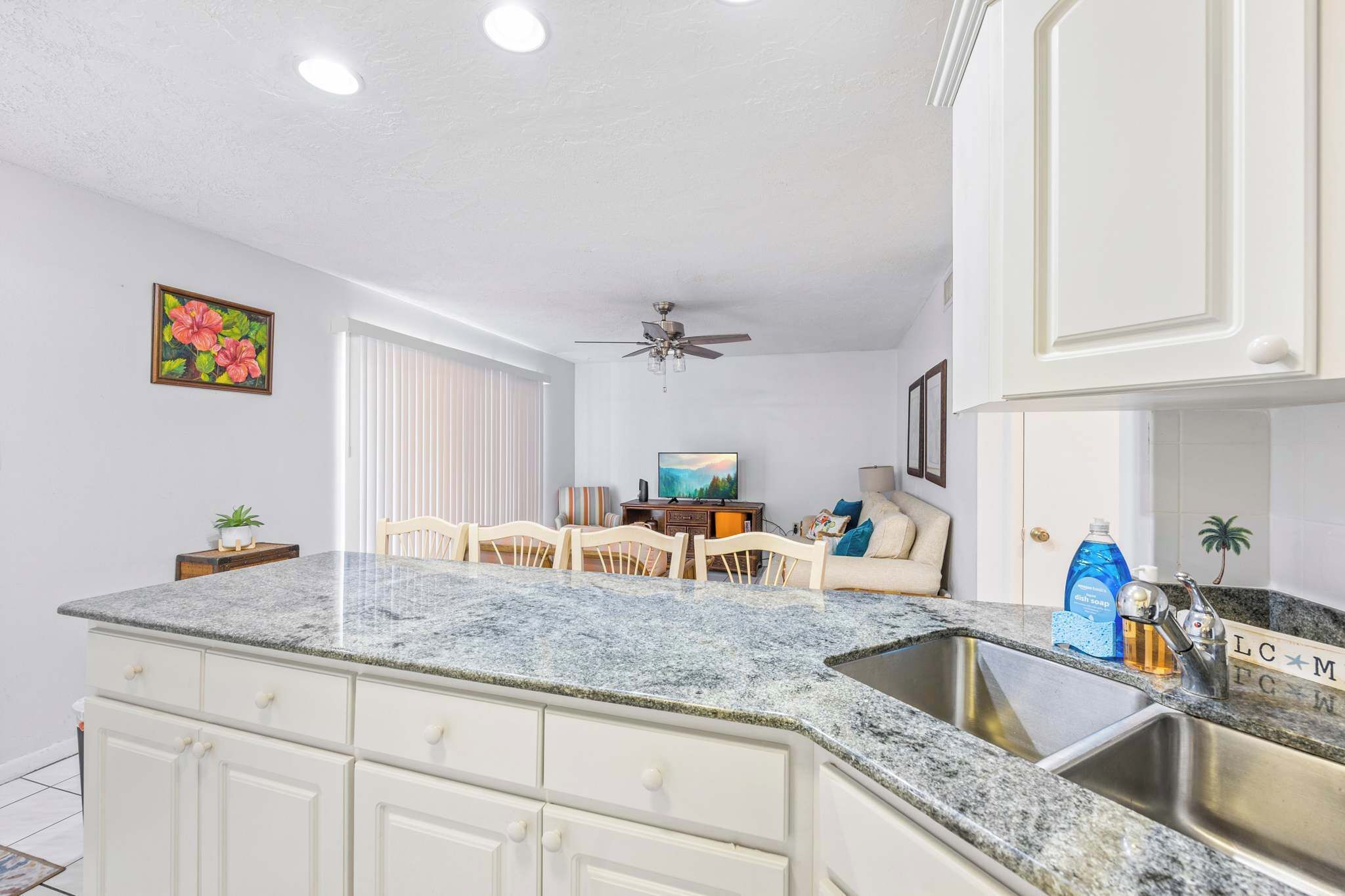 A kitchen with a granite countertop, white cabinets, a ceiling fan, and a dining area with a table and chairs.