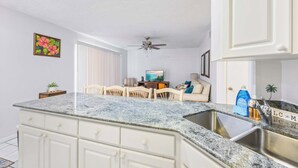A kitchen with a granite countertop, white cabinets, a ceiling fan, and a dining area with a table and chairs.