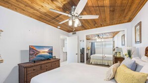 A bedroom with a large bed, a ceiling fan, a television on a dresser, and a mirror reflecting the room.