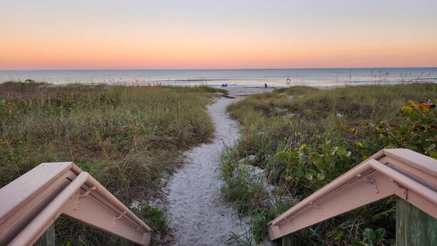 A beach path leading to the sea with a lifeguard tower in the distance.