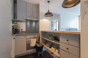 A compact kitchen with a stove, oven, and a small trash bin.
