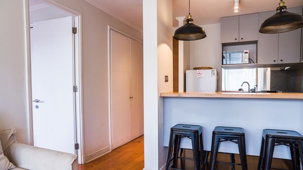 Una cocina moderna con un microondas, un lavamanos y tres taburetes negros.