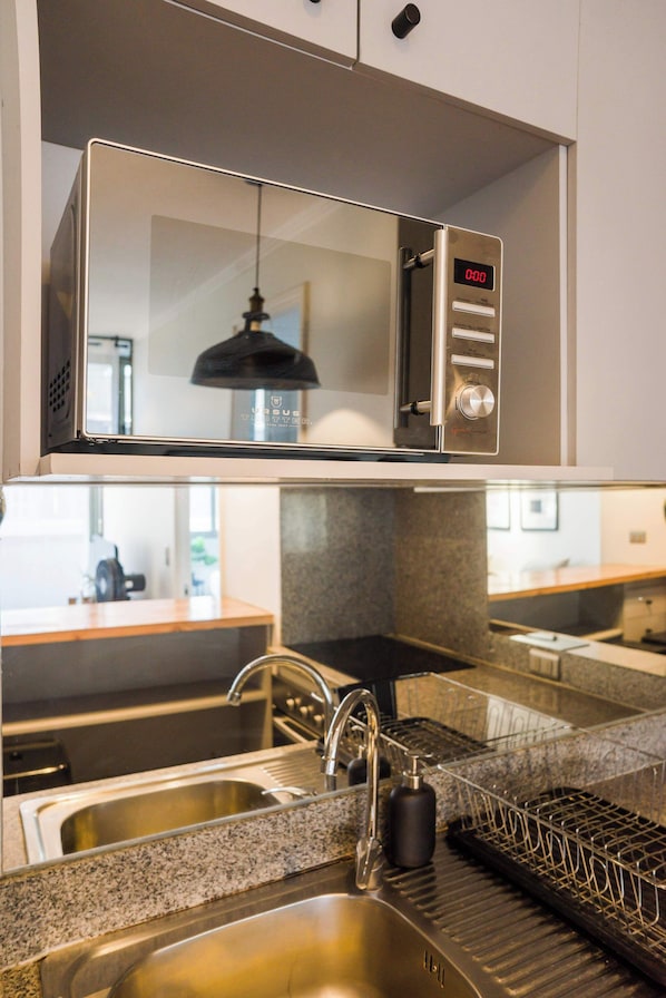 A kitchen with a stainless steel microwave, a sink with a faucet, and a dish rack.