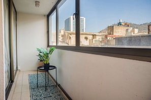 A balcony with a potted plant, a small table, and a view of buildings.