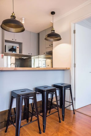 A kitchen with a microwave, double sink, and two bar stools.