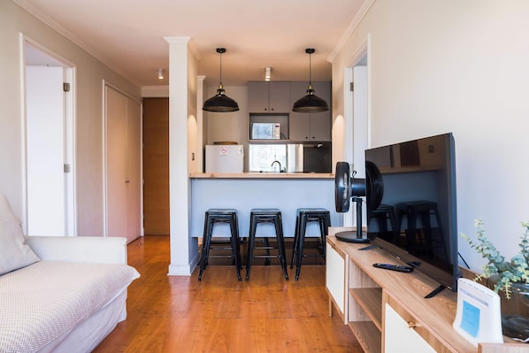 A compact living space with a kitchenette, a sofa, a TV, and a fan.