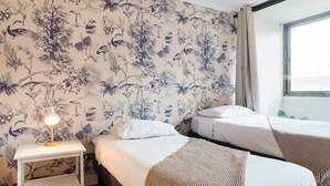 Una habitación de hotel con dos camas, una mesita de noche con lámpara y un papel tapiz floral.