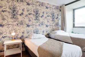 Una habitación de hotel con dos camas, una mesita de noche con lámpara y un papel tapiz floral.
