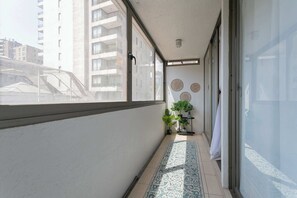 A narrow balcony with a tiled floor, a potted plant, and a wall-mounted shelf.