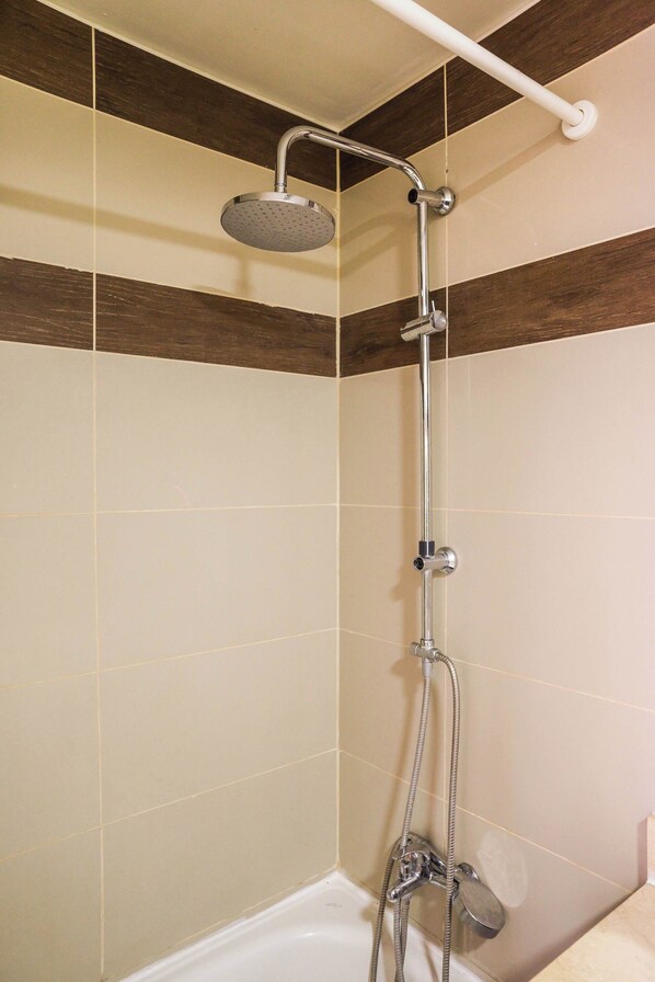 A shower with a handheld showerhead, a wall-mounted faucet, and a handheld hose.