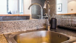 Una cocina con pileta de acero inoxidable, encimera de granito y escurridor de platos.