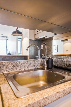 Una cocina con pileta de acero inoxidable, encimera de granito y escurridor de platos.