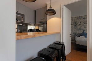 A compact kitchen with modern appliances, a wooden countertop, and black stools.