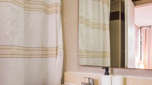 Une salle de bain équipée d’un rideau de douche, d’un lavabo, d’un miroir et d’un porte-rouleau de papier toilette.