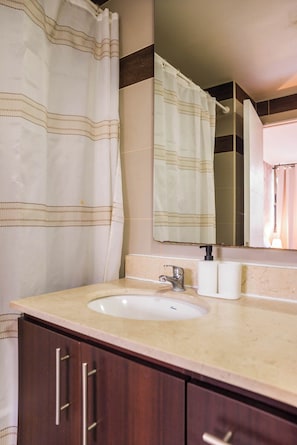A bathroom with a shower curtain, a sink, a mirror, and a toilet paper dispenser.