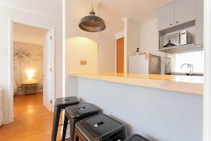 A kitchen with a wooden countertop, black stools, a hanging light fixture, and a refrigerator.