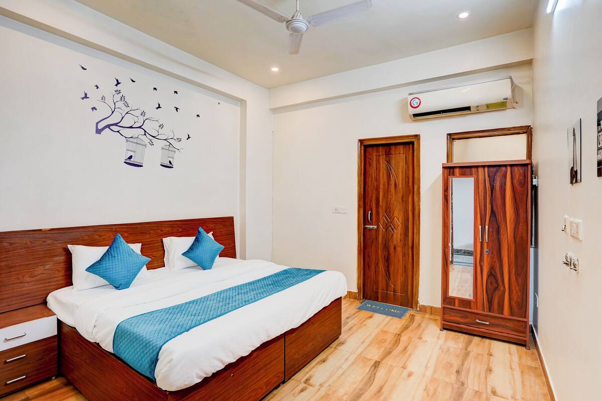 A bedroom with a wooden bed, white and blue bedding, a ceiling fan, an air conditioning unit, and wooden wardrobes.