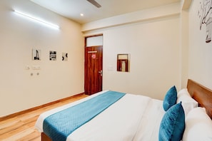 A bedroom with a wooden floor, a bed with a blue quilt, and a wooden door. - Axel Accommodation (Noida)
