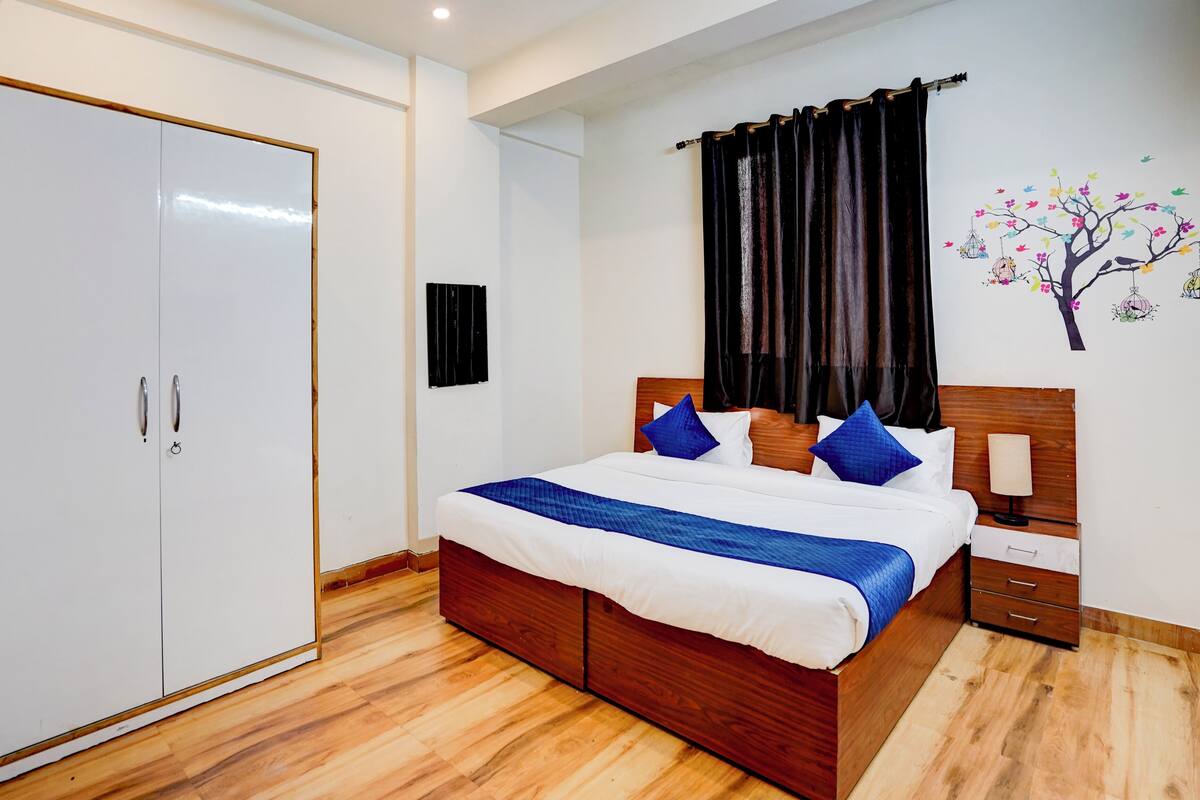 A hotel room with a wooden bed, white walls, a wardrobe, and a wall-mounted TV.
