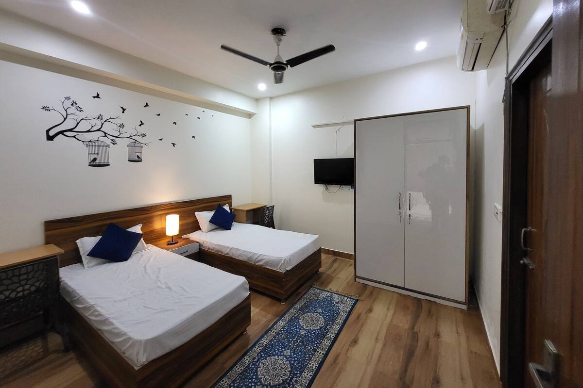 A hotel room with two beds, a ceiling fan, a TV, and a wardrobe.
