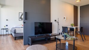 A modern hotel room with a large flat-screen TV, a bed, a small table with chairs, and a potted plant. - Chic 2BR Apt in Las Condes with Pool & Views (Santiago)