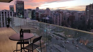 A balcony with a city view at sunset, featuring modern buildings and a glass railing. - Chic 2BR Apt in Las Condes with Pool & Views (Santiago)