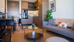 A modern living room with a glass coffee table, a grey sofa, and a kitchen in the background. - Chic 2BR Apt in Las Condes with Pool & Views (Santiago)