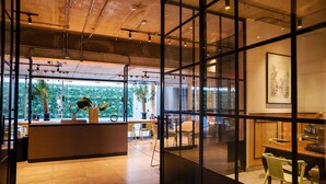An interior space with a reception desk, seating area, and large windows offering a view of greenery. - Chic 2BR Apt in Las Condes with Pool & Views (Santiago)