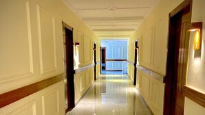 Un largo pasillo bien iluminado con suelo de mármol y paneles de madera en las paredes.